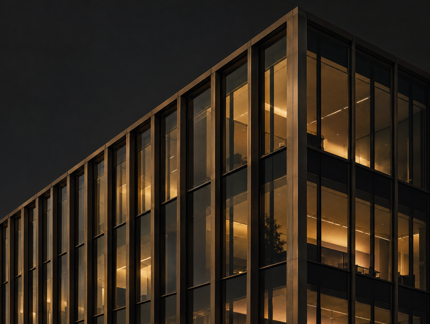 The illuminated glass corner of a modern office building at dusk